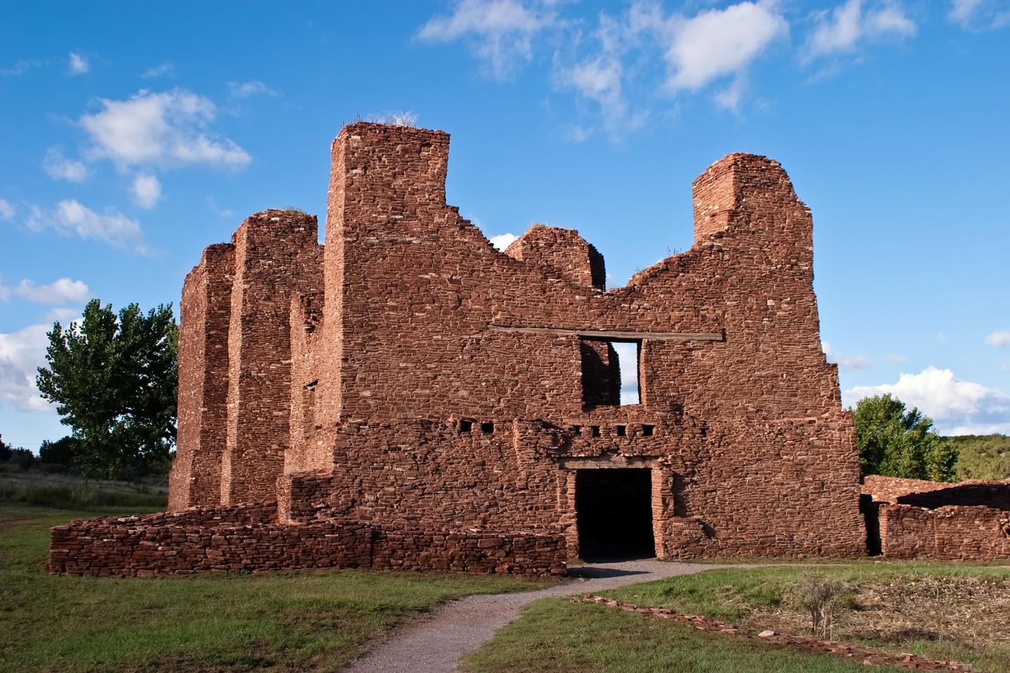 Ancient red stone ruins under a blue sky with scattered clouds.