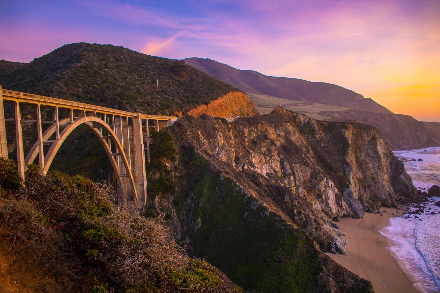 Dramatic coastline with a bridge at sunset, cliffs, and ocean waves.