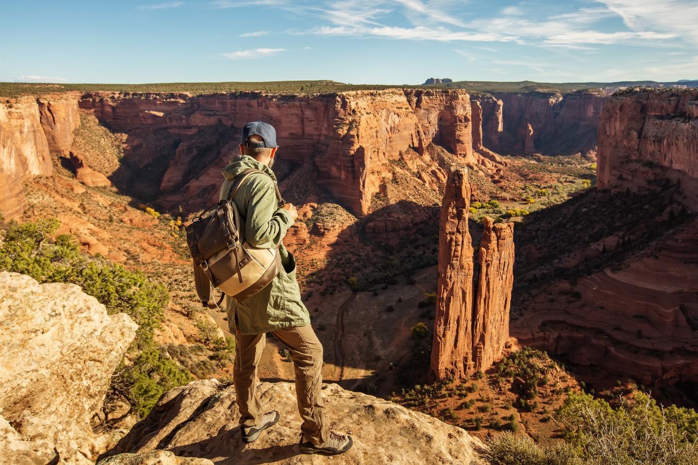 Hiker gazing at a sunlit Canyon de Chelly with tall rock formations.