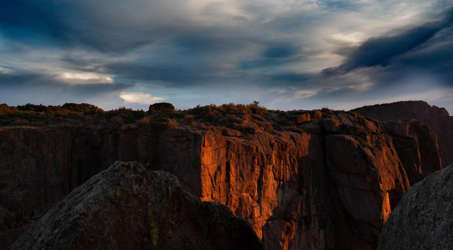 Sunlit rock faces under a moody sky at sunset.