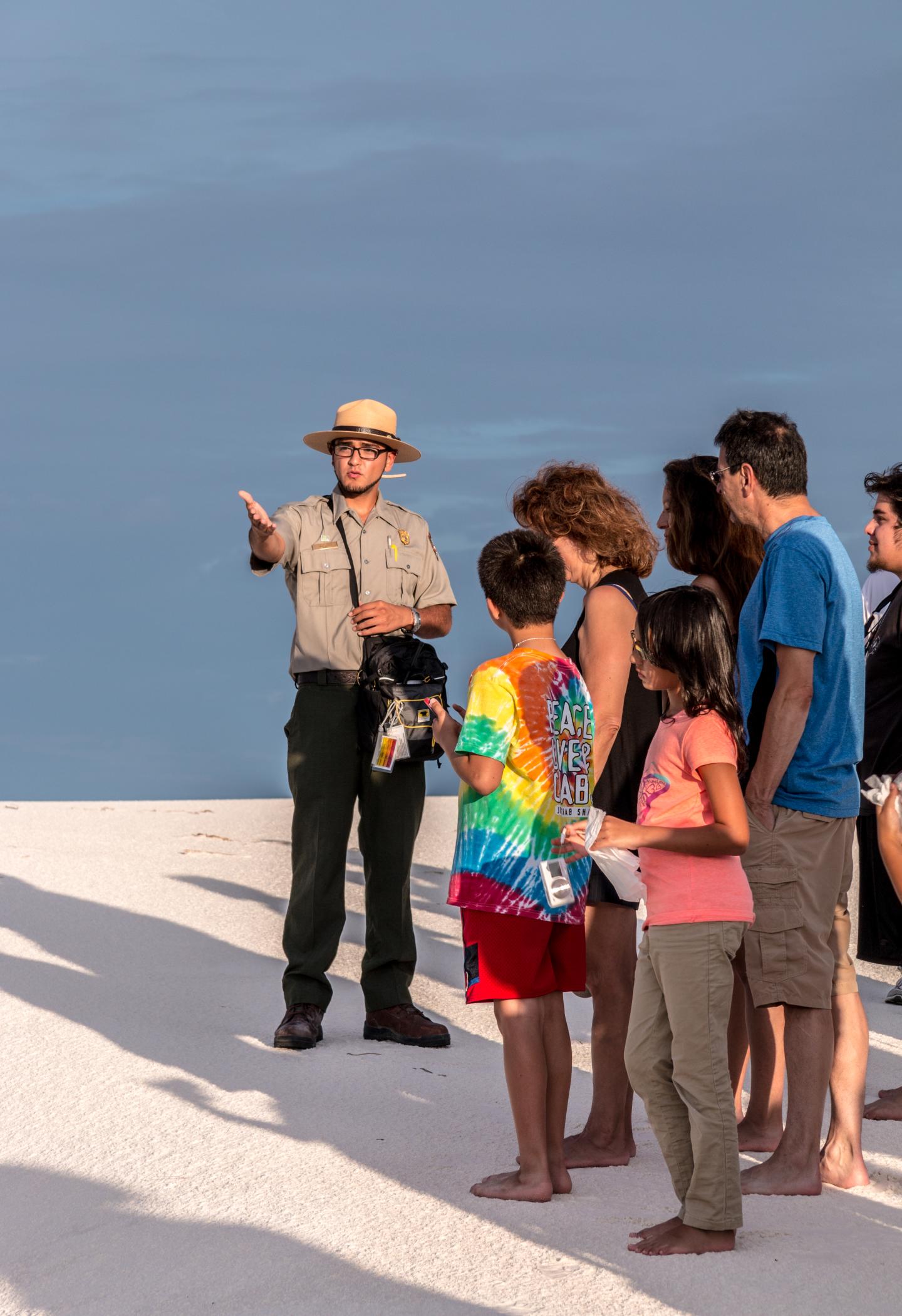 Park ranger talks to a group on a sandy area under a clear sky at White Sands National Park