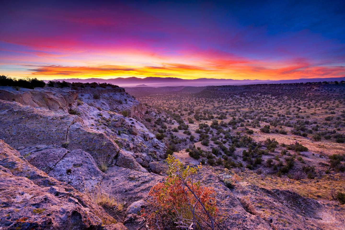 Colorful desert sunset over a rocky landscape with distant mountains.