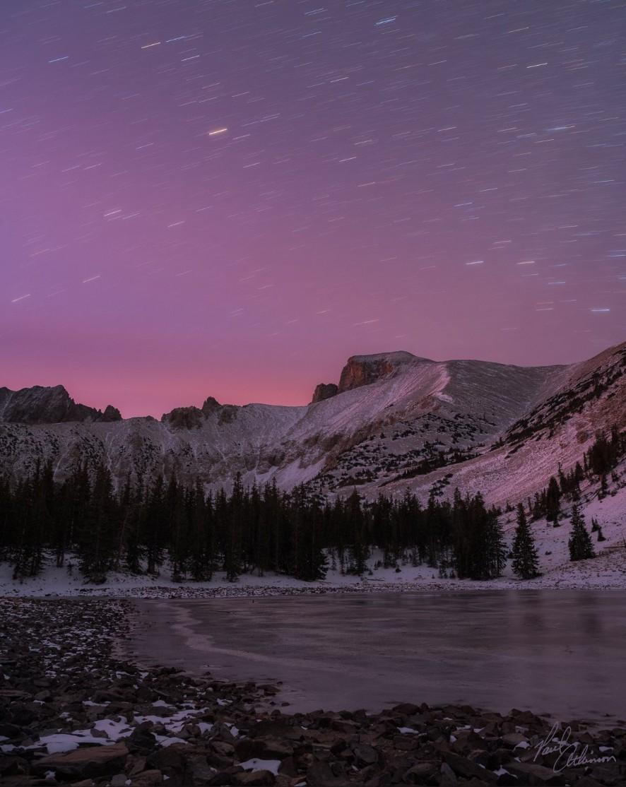 Snow-covered mountains under a starry purple sky at dusk.