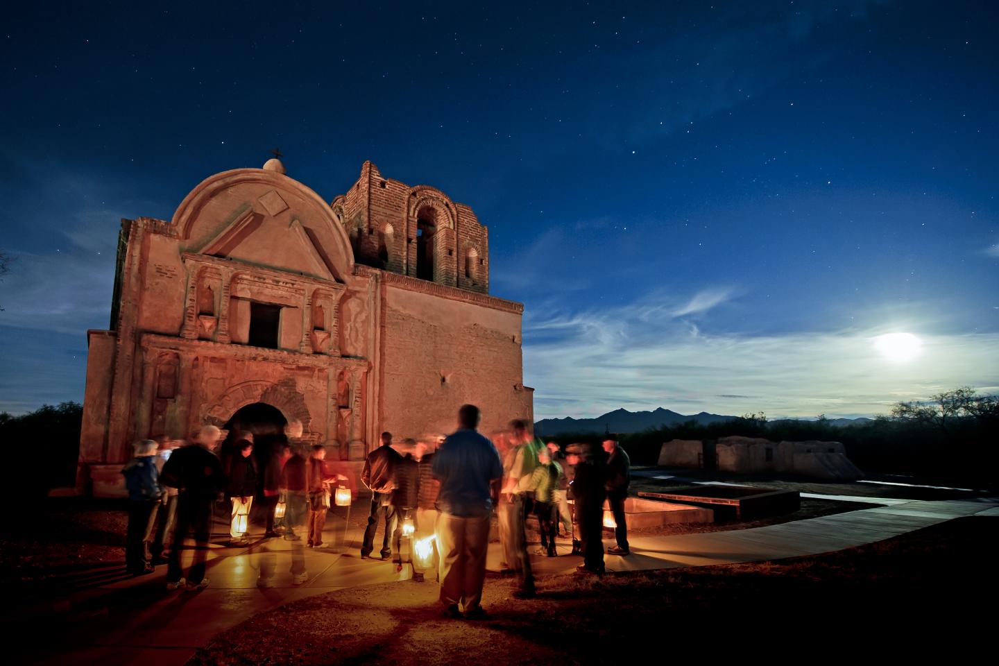 People gathered by a building, moonlit sky above.