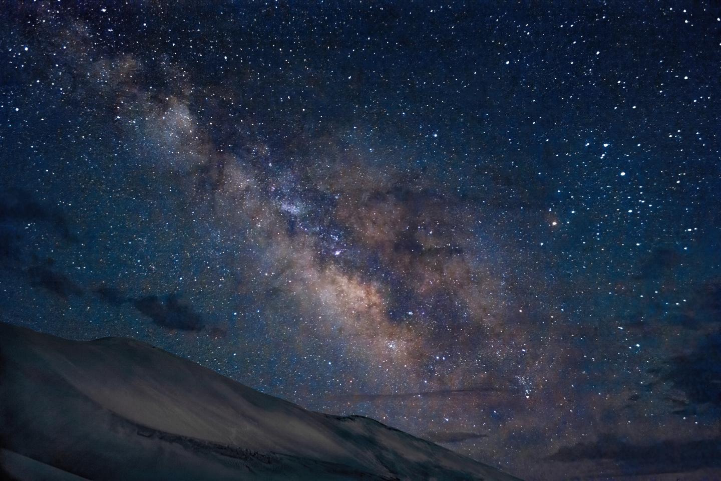 Starry night sky with the Milky Way over dark silhouetted mountains.