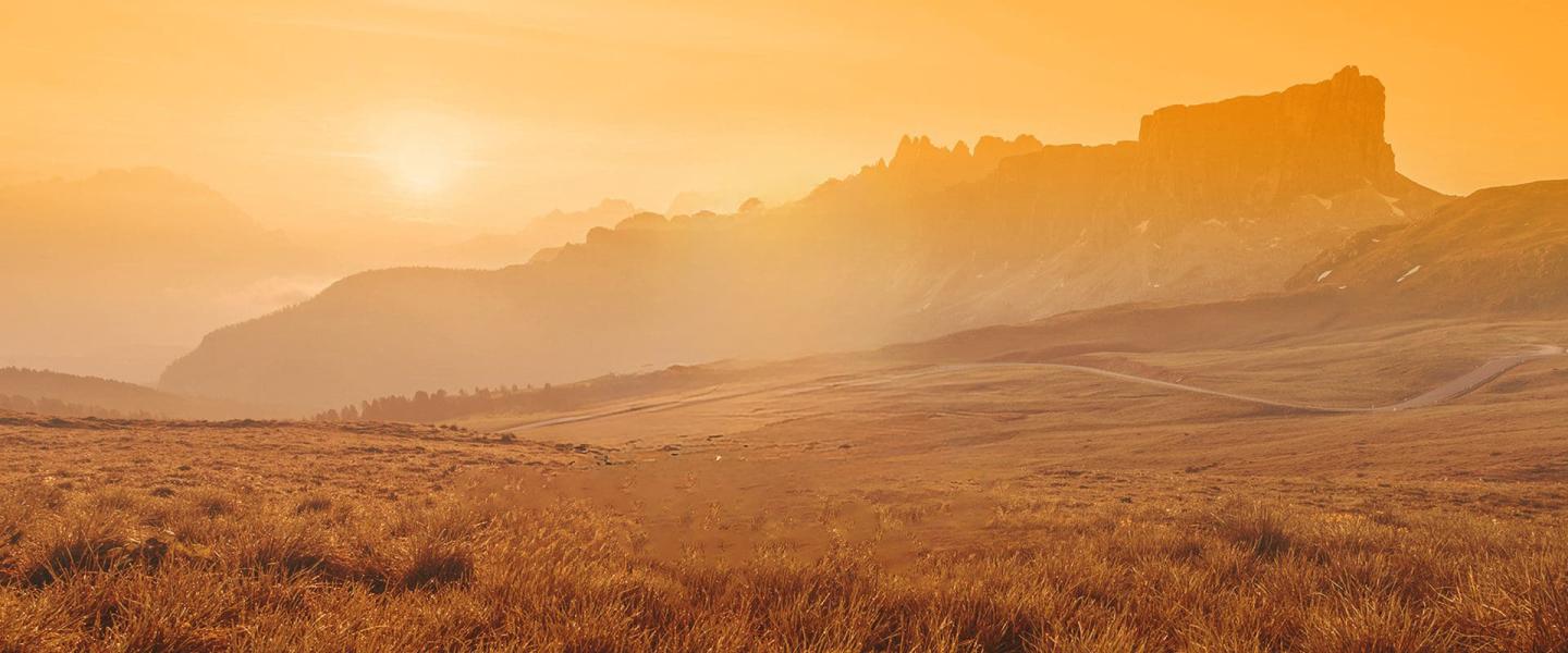 Golden sunset over a grassy field and distant mountains.