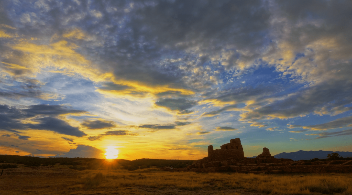 Sunset over a desert landscape with dramatic clouds and rock formations.