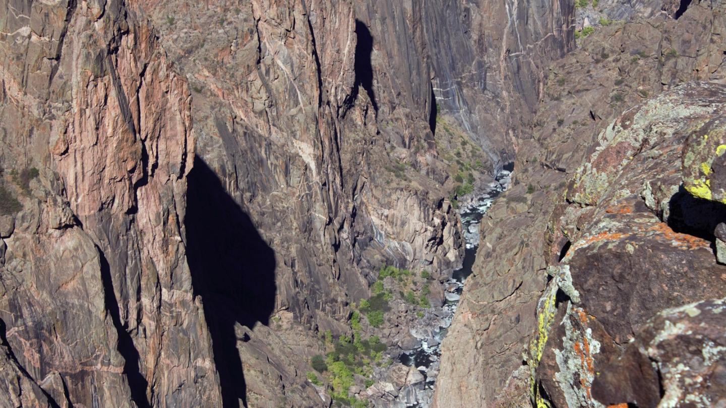 Steep rocky canyon with a river and sparse greenery.