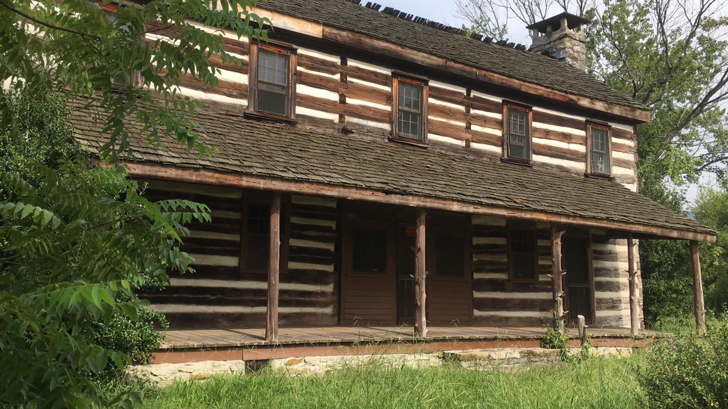 Trail of Tears log cabin with a wooden porch surrounded by greenery.