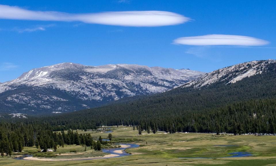 Snow-capped mountains, lush green valley, and blue sky with white clouds.