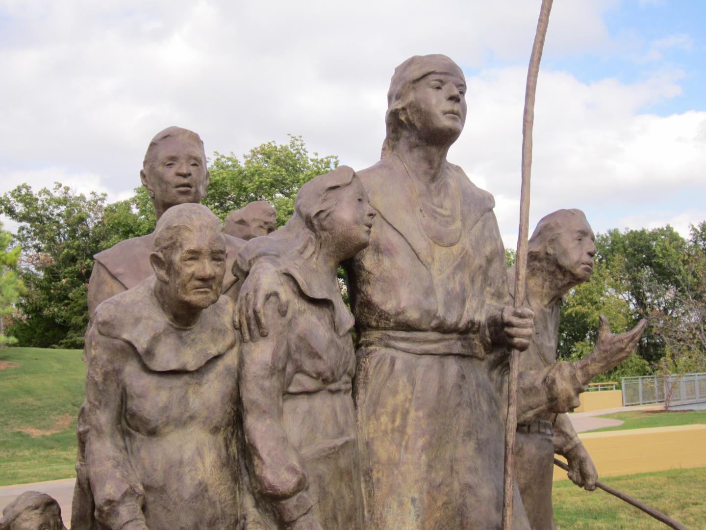 Bronze sculpture of six people standing together outdoors at Chickasaw Cultural Center.