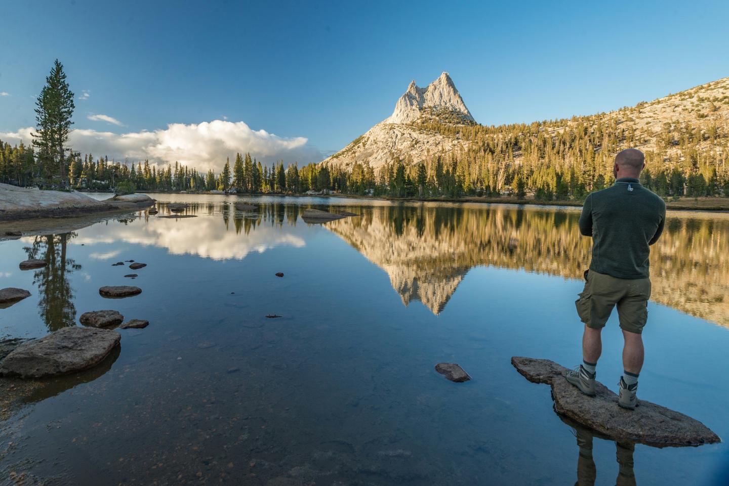 Person standing on rock, overlooking Cathedral Lake with mountains reflected.