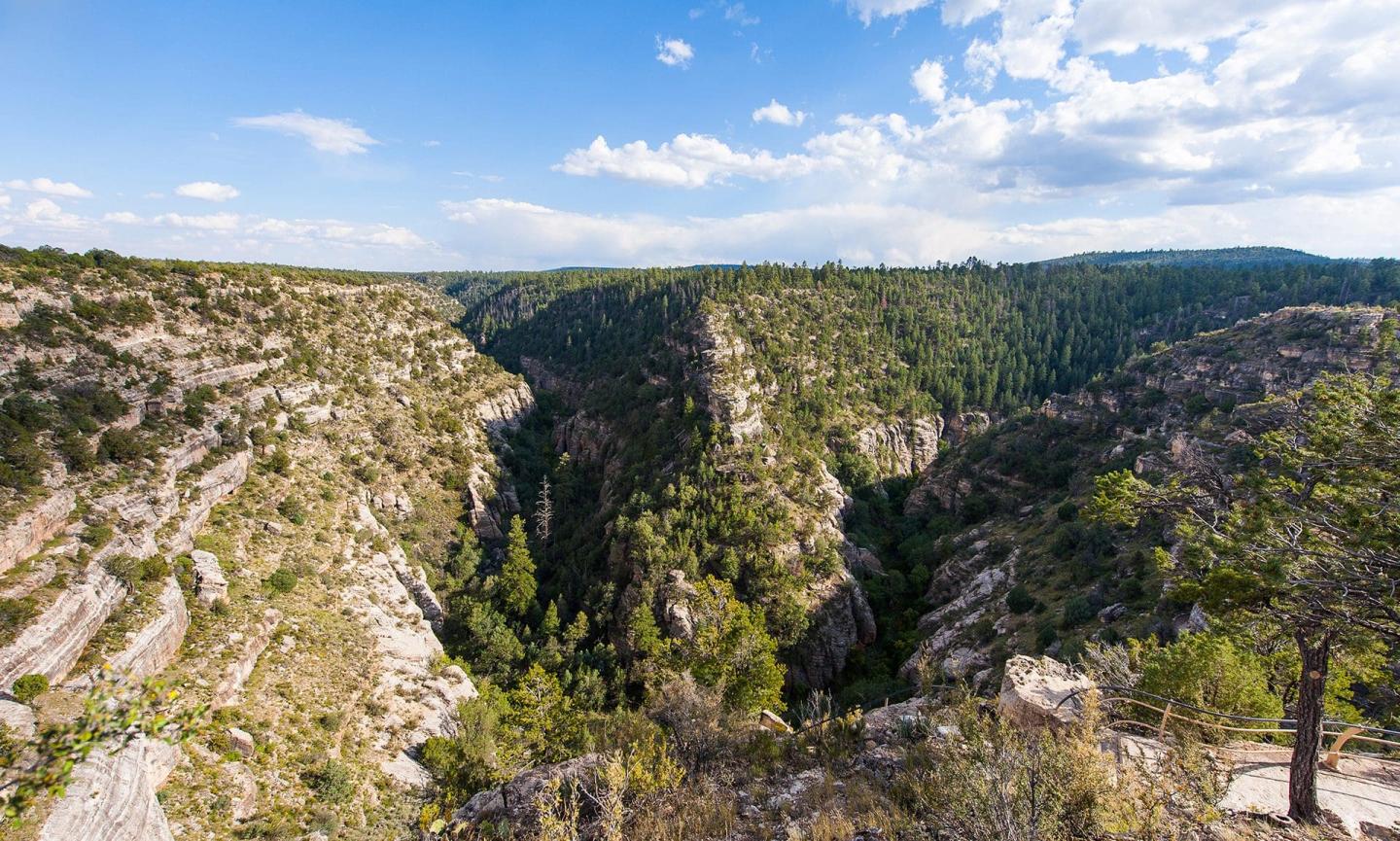 Walnut Canyon landscape under a bright blue sky with scattered clouds.