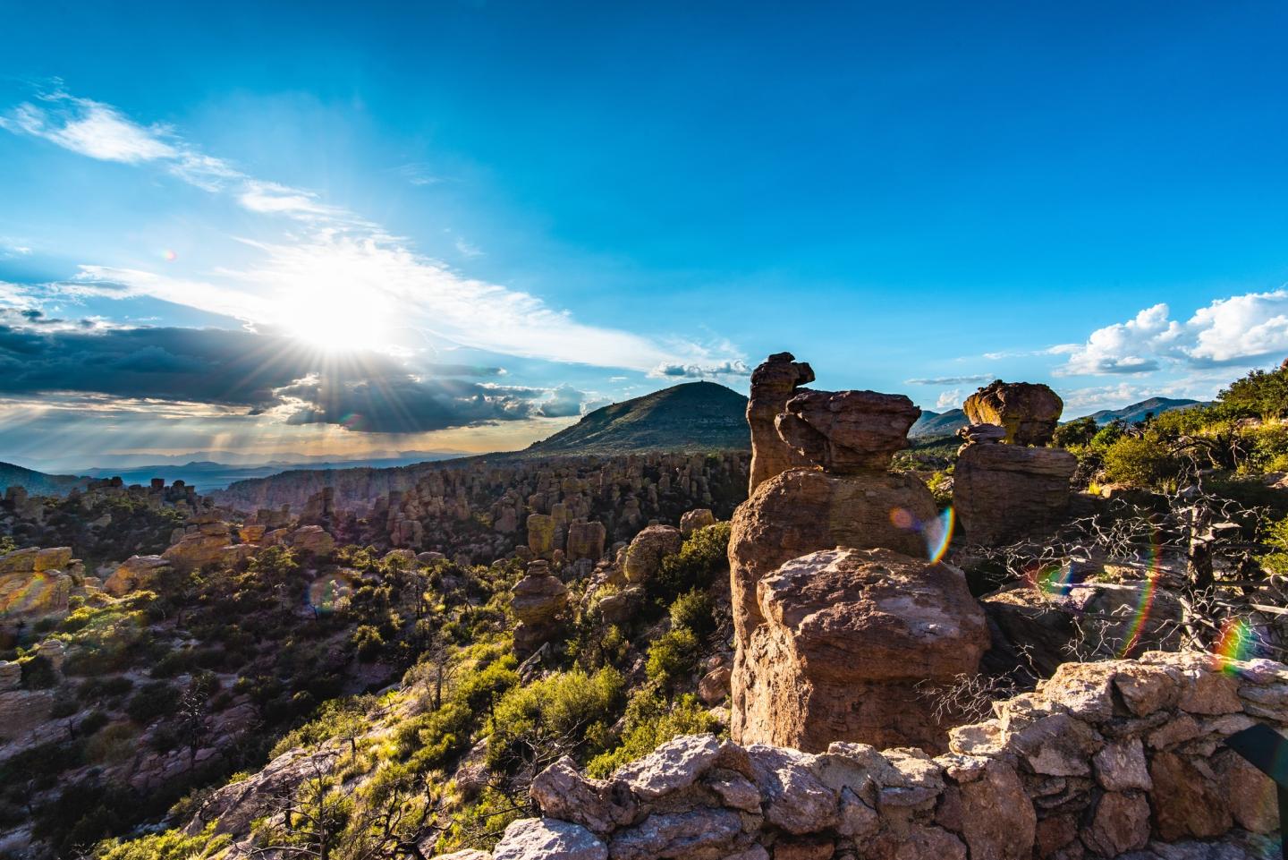 Rocky landscape under a bright blue sky with sun rays and distant mountains.