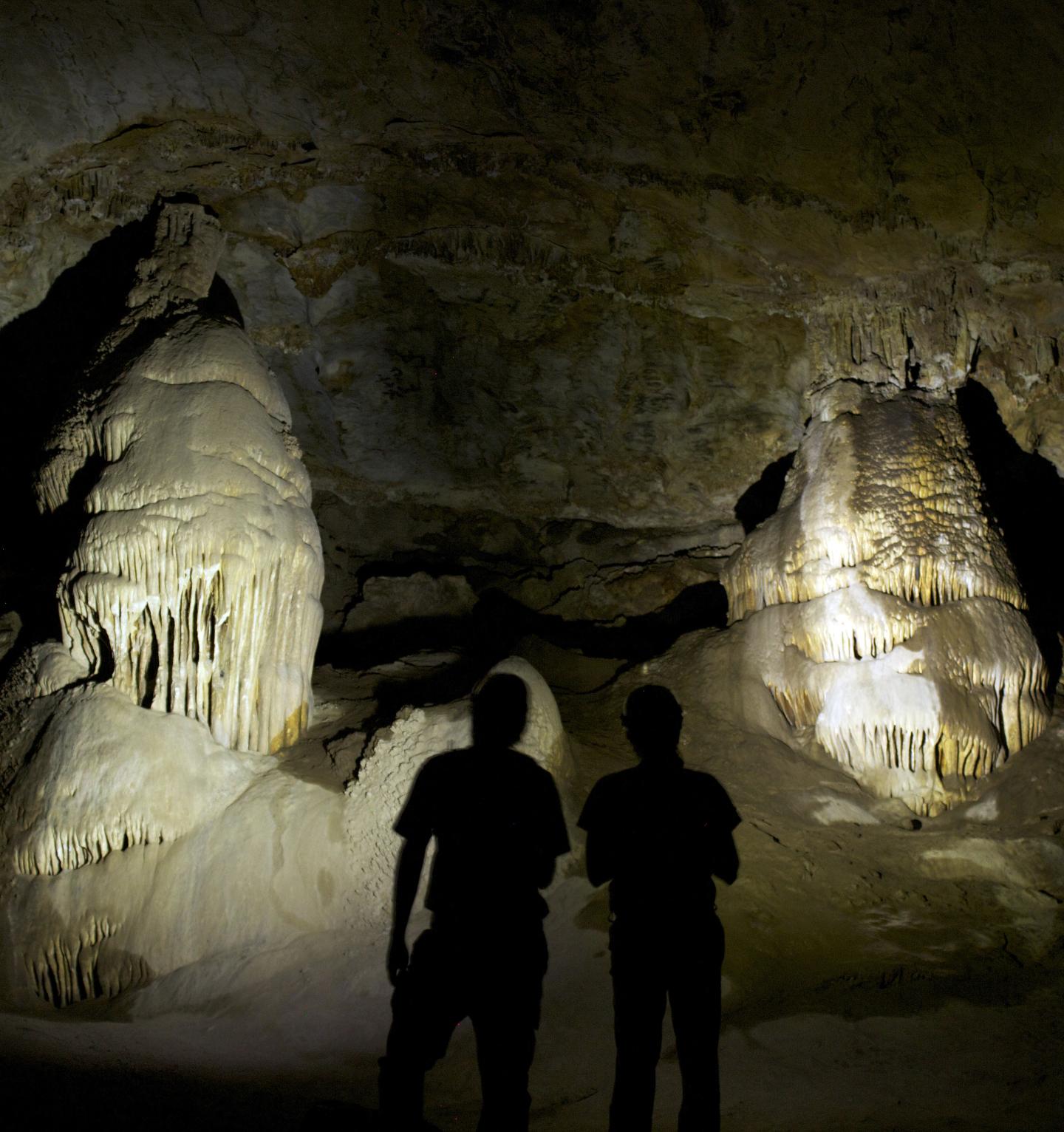 Cave with two people silhouetted against stalagmites.