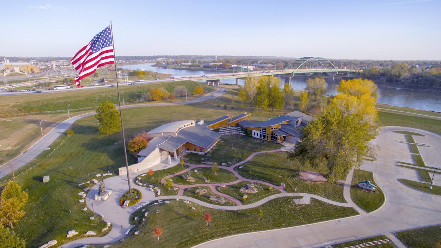 Aerial view of Lewis & Clark Interpretive Center, with a large American flag, paths, and trees by a river.