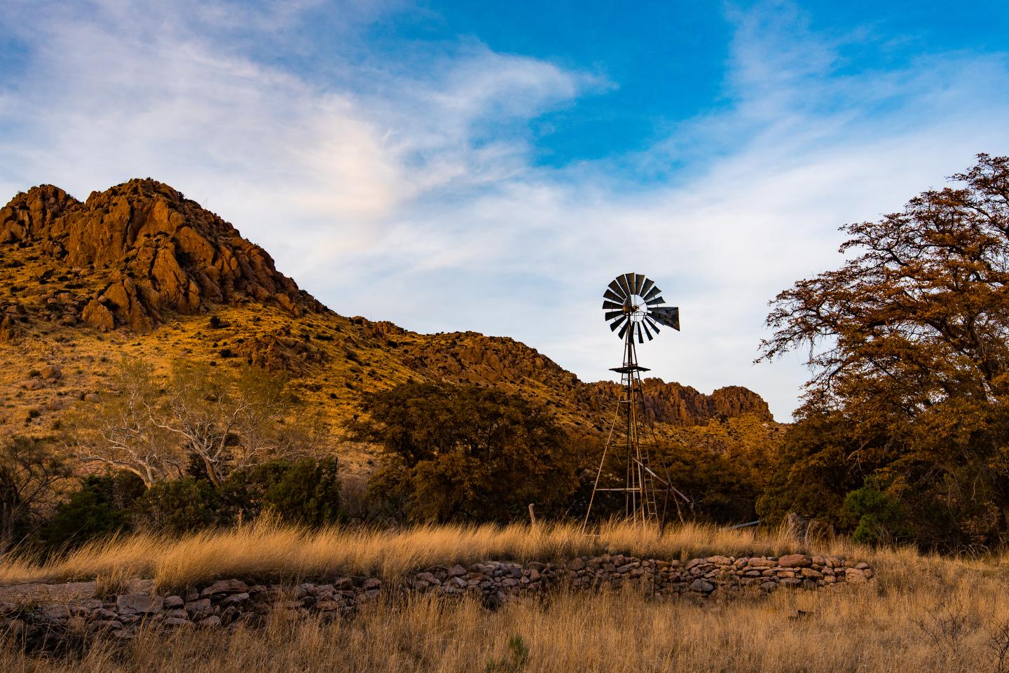 Windmill in a grassy landscape with mountains and a blue sky.