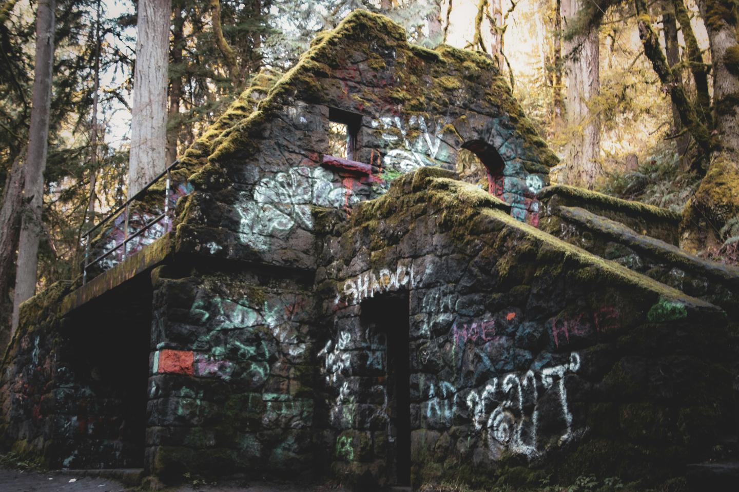 Moss-covered stone building with graffiti in a forest setting.