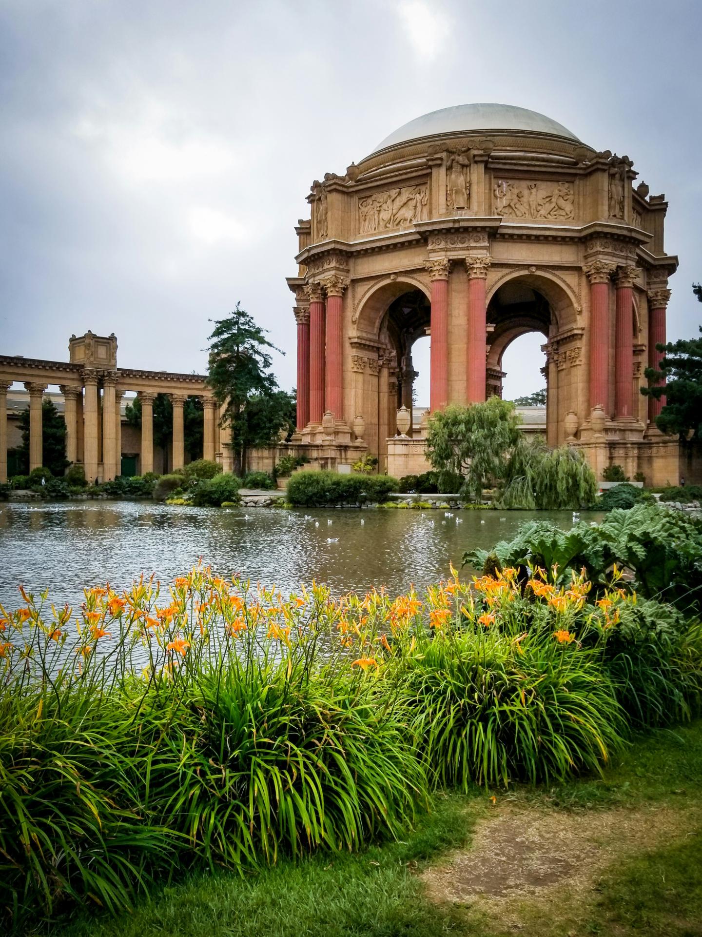 Grand rotunda at the Palace of Fine Arts by a pond with orange flowers and lush greenery.