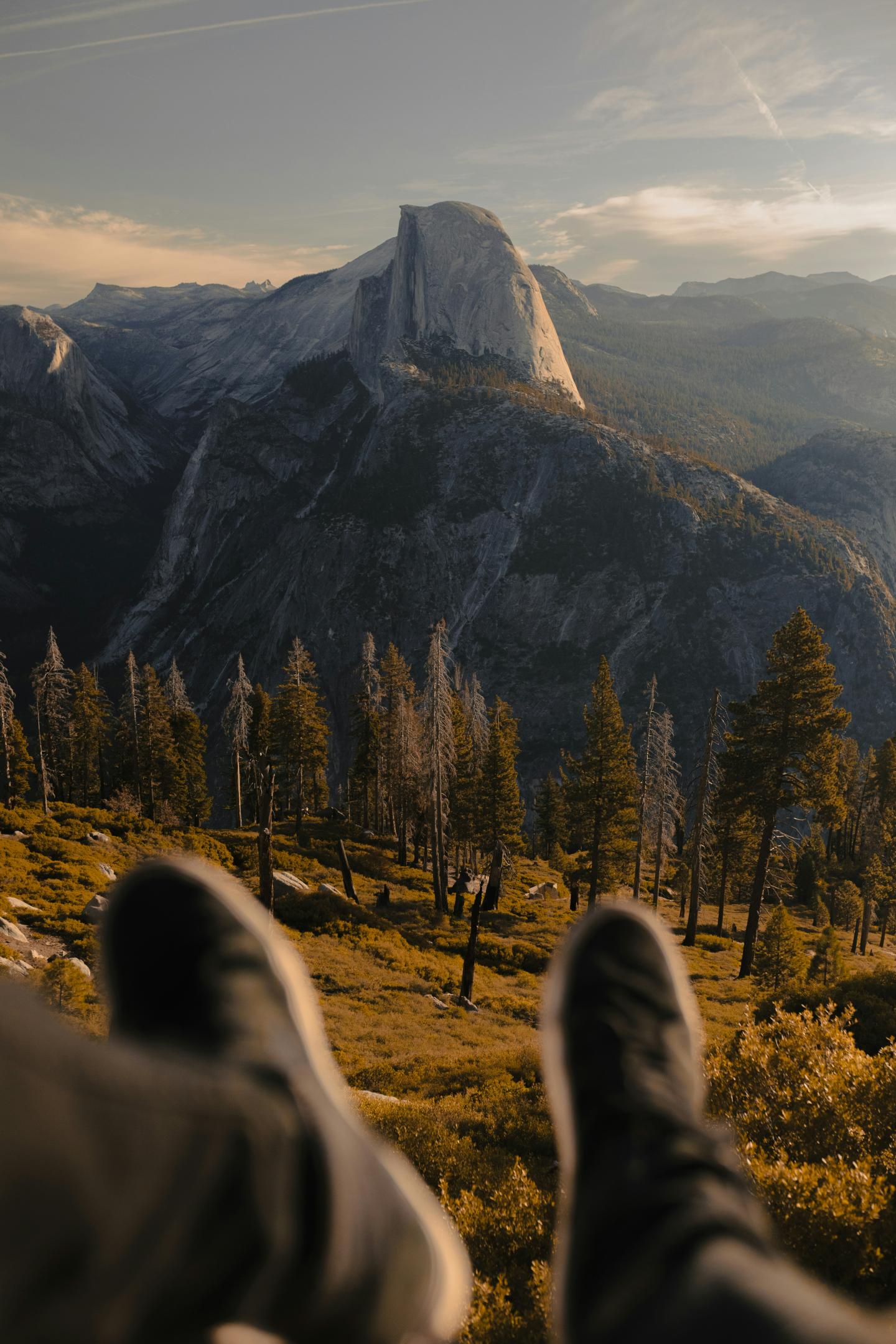 Feet in foreground, overlooking distant mountains and trees at sunset.