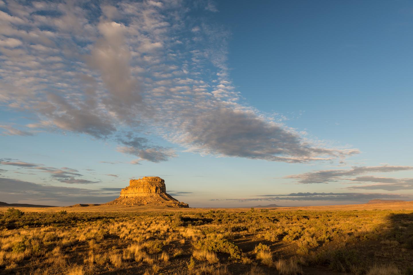 Desert landscape with a distant rock formation under a partly cloudy sky at sunset.