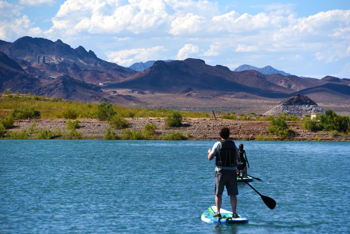 Two people paddleboarding on a lake with mountains in the background.