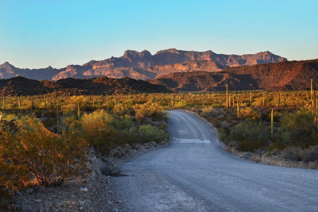 Desert road with distant mountains under a clear blue sky.