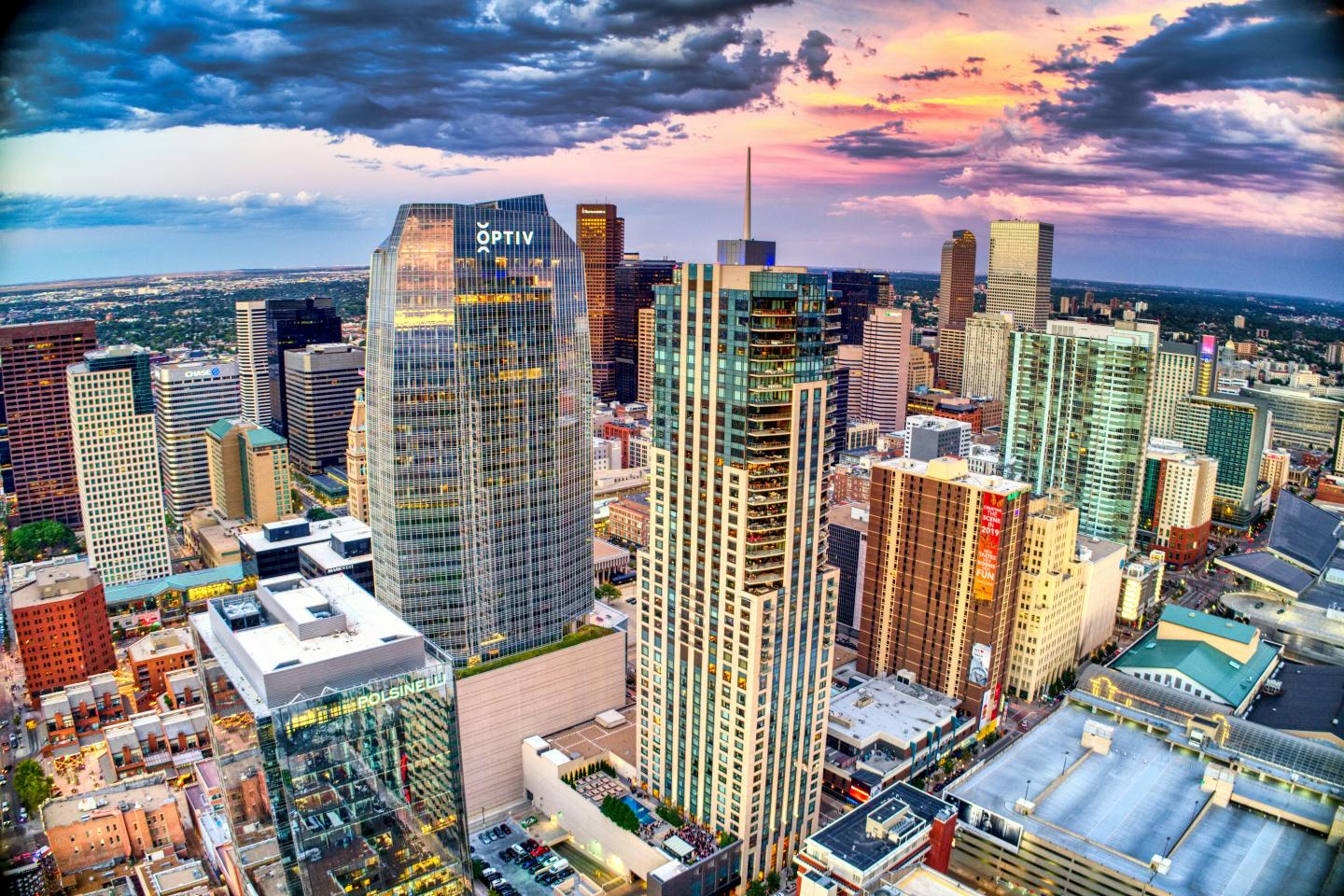 Colorful Denver skyline at sunset with tall buildings and a dramatic sky.