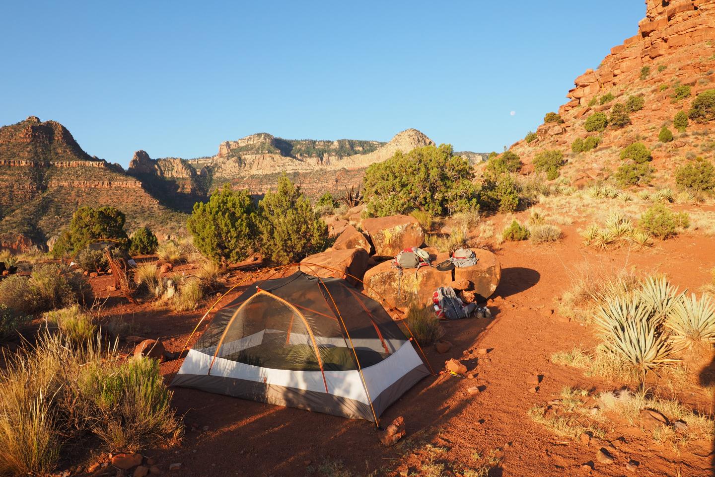 Tent on rocky desert landscape with mountains under clear sky.