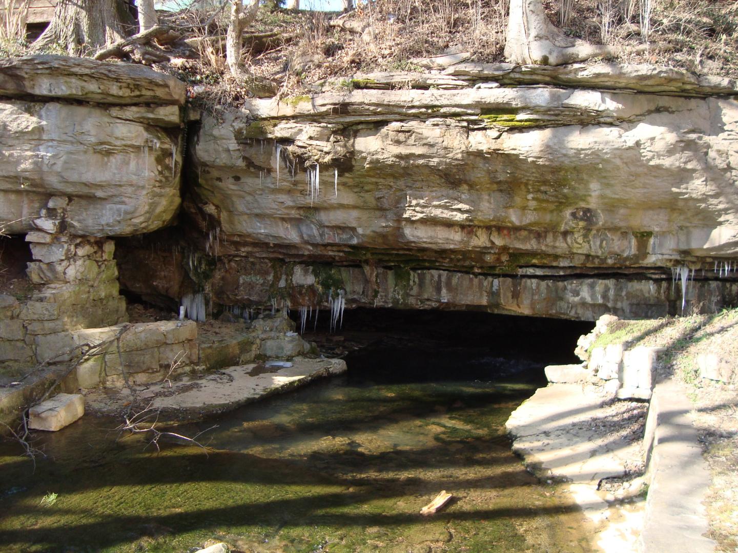 Rocky cave entrance with icicles and shallow water below.