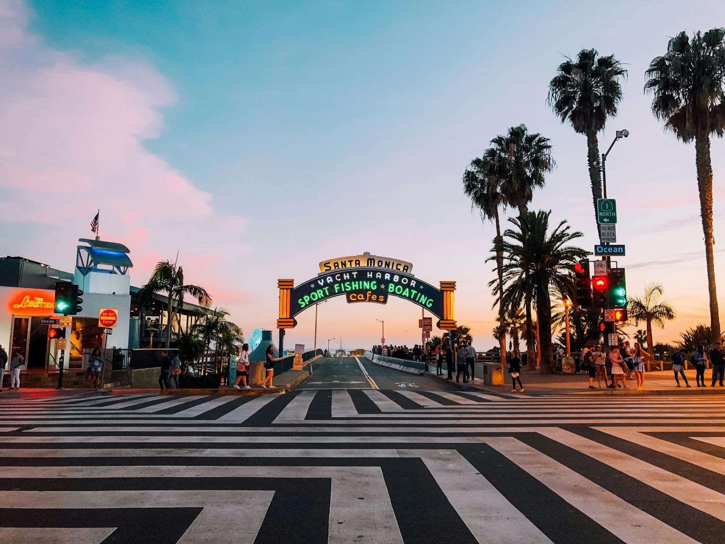 Santa Monica Pier entrance at sunset with palm trees and colorful sky.