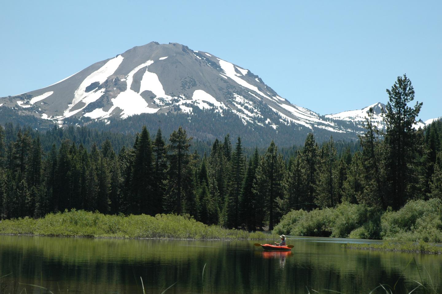 Kayaker on lake in Lassen Volcanic National Park and pine trees.