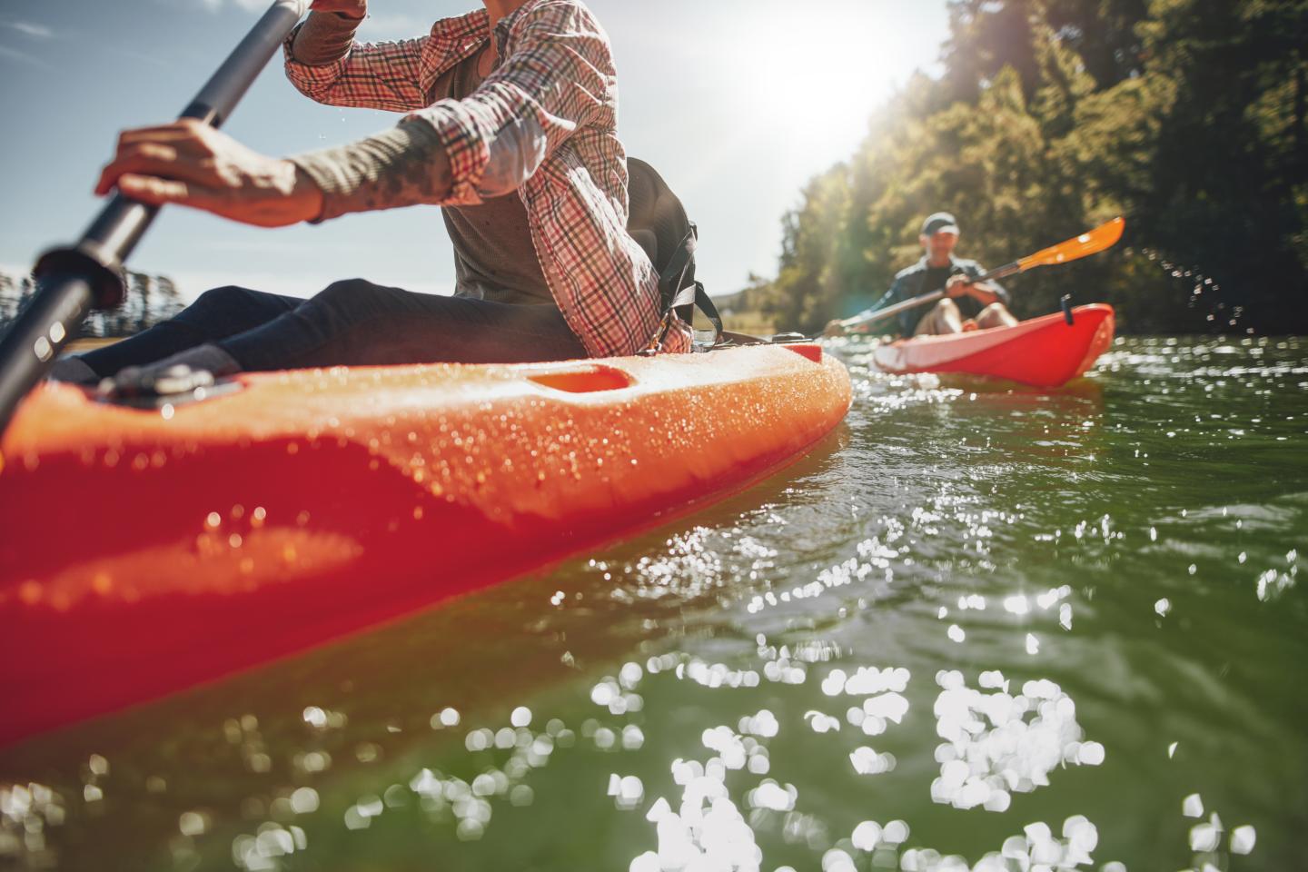 Two kayakers paddling on a sunny river, close-up on the red kayak.
