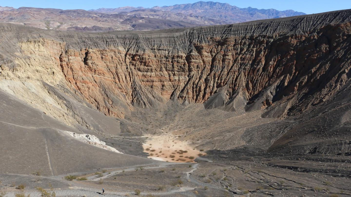 Steep desert crater with layered rock formations under a clear blue sky.