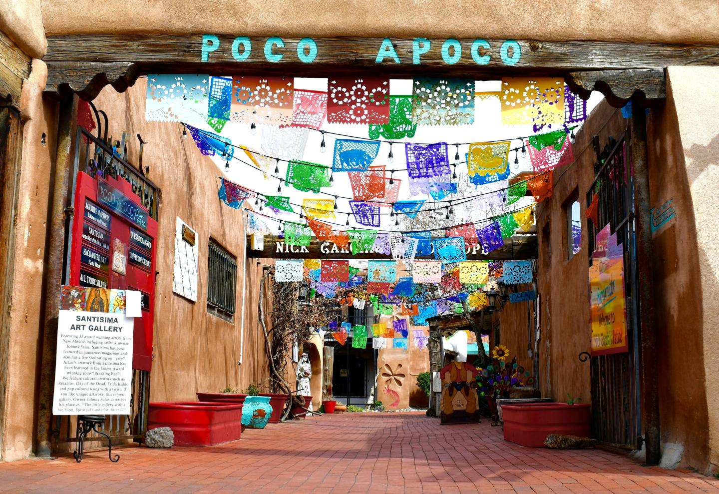Colorful flags and signs in a sunlit courtyard entrance.