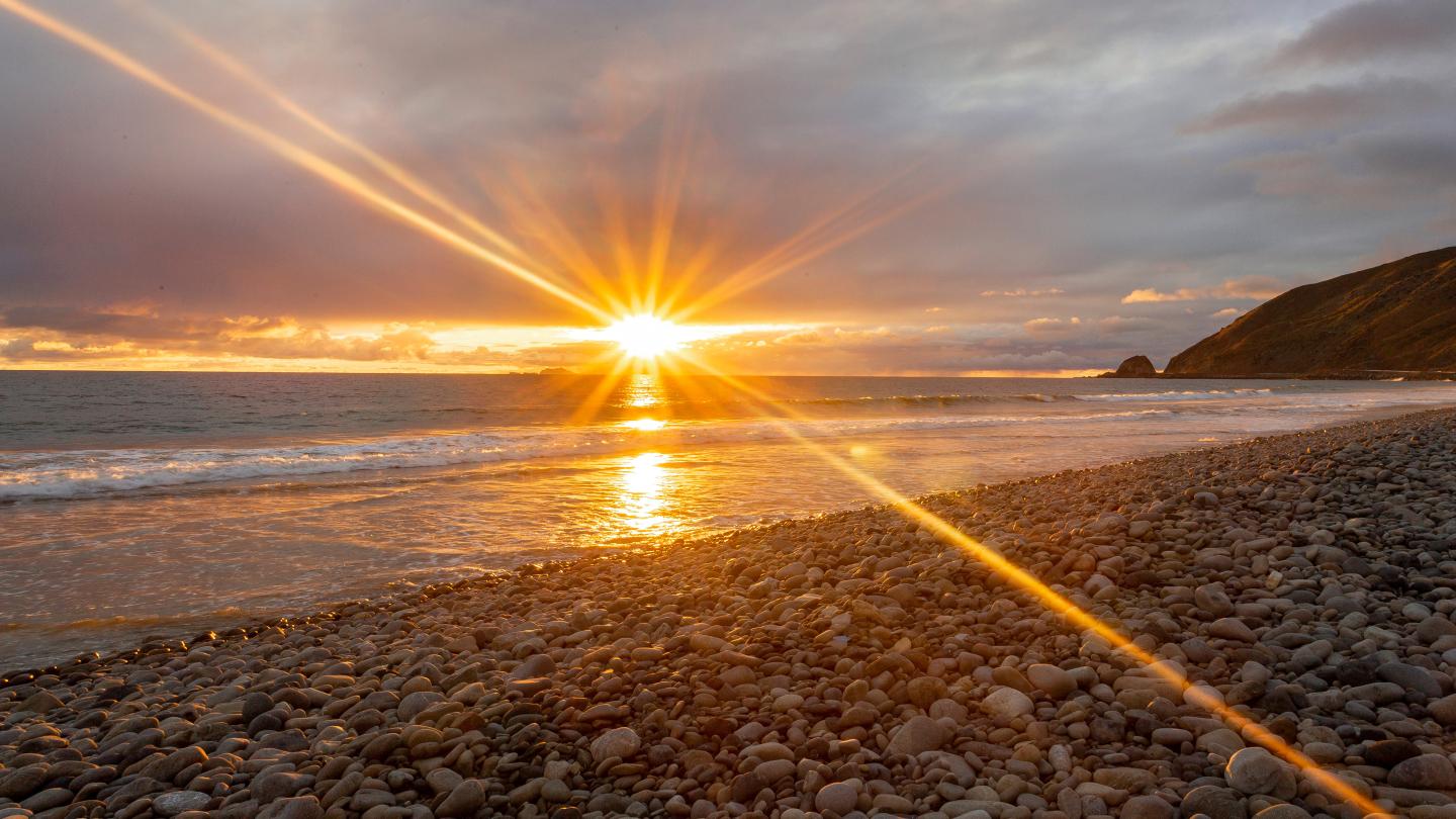 Rocky beach at sunset with sun rays reflecting on the water.