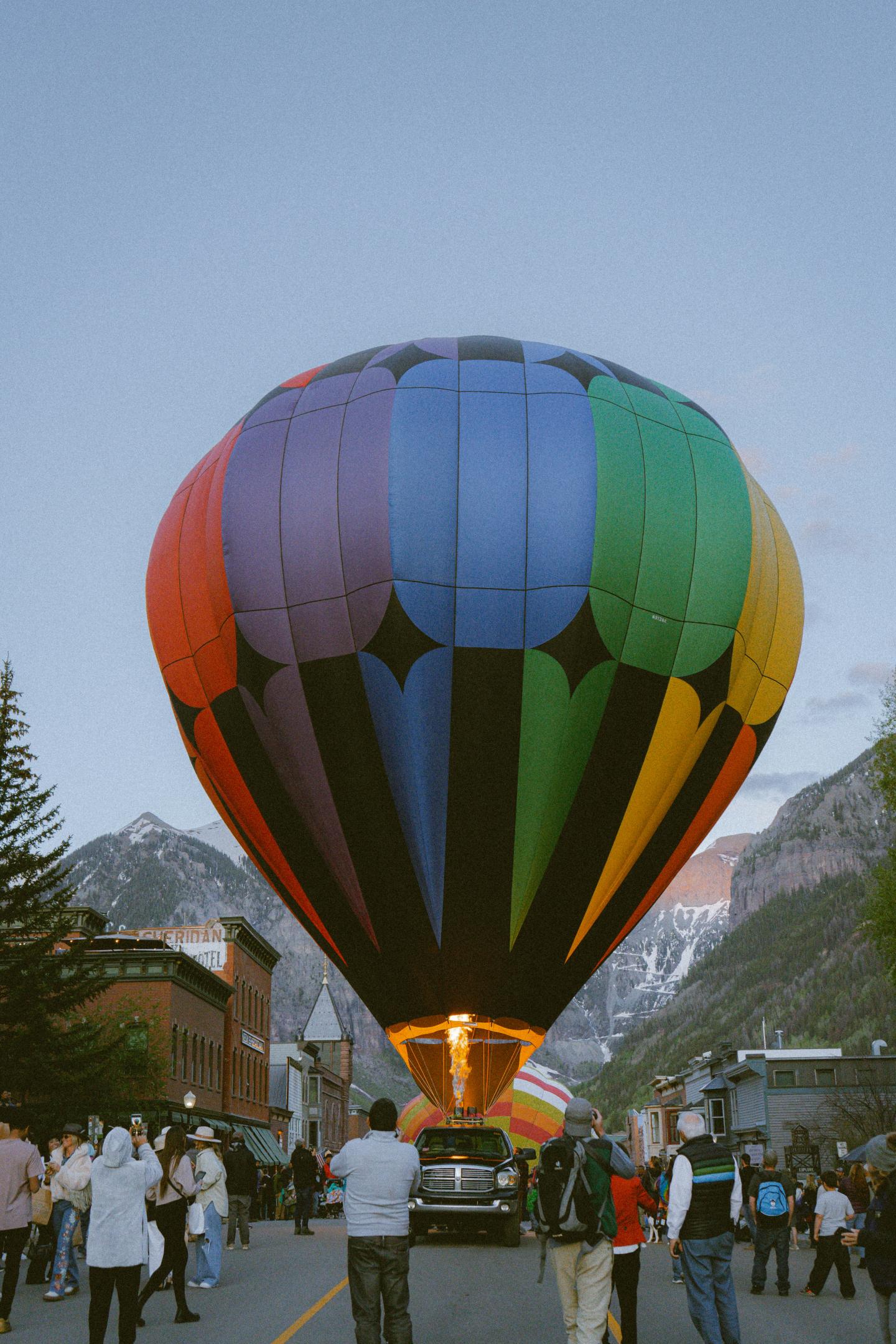 Colorful hot air balloon on a street, mountains in background, people watching.