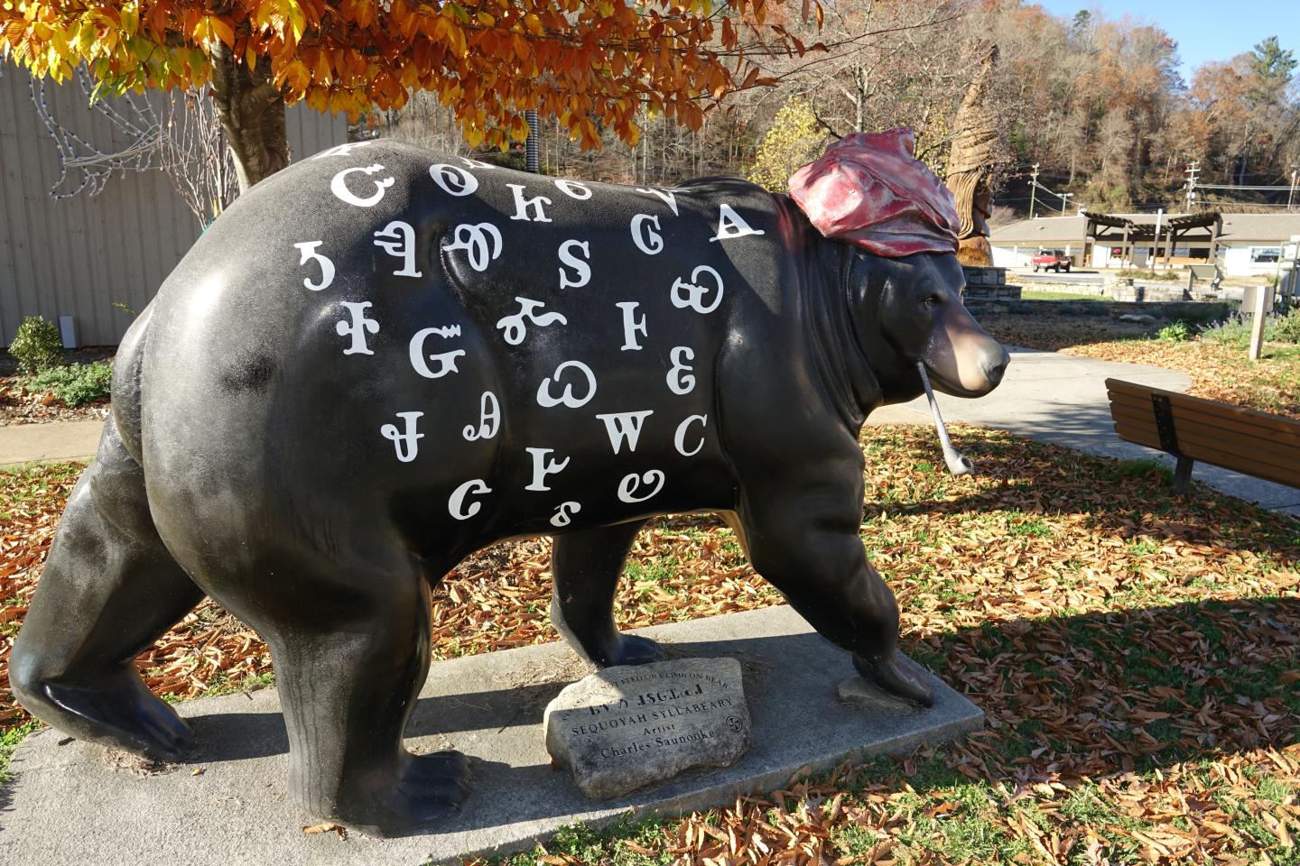 Sculpture of a bear with symbols, wearing a hat, in an outdoor park setting.