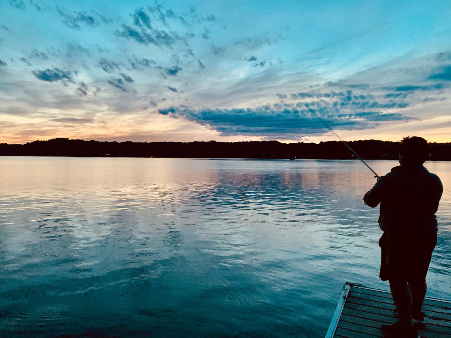 Person fishing at sunset on a calm lake.