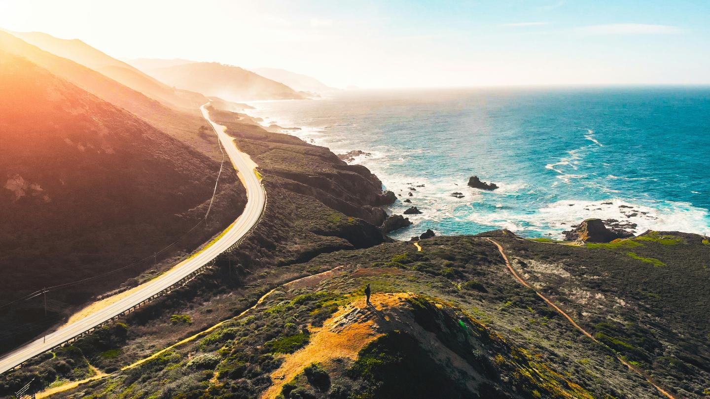 Coastal California road with cliffs and ocean under a clear blue sky.