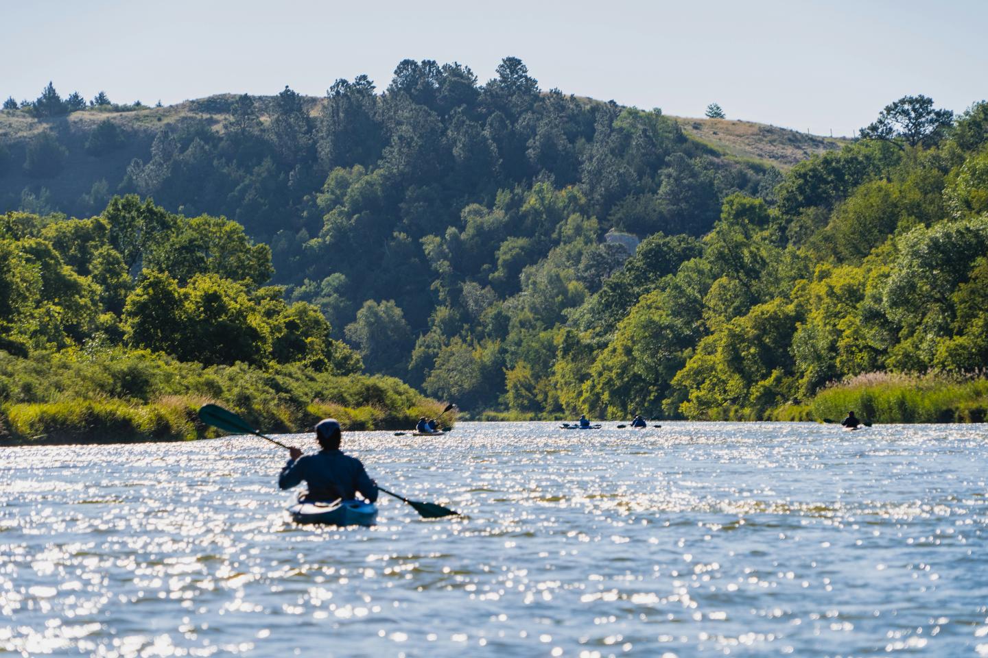 Kayaker paddling on a river surrounded by lush green hills.