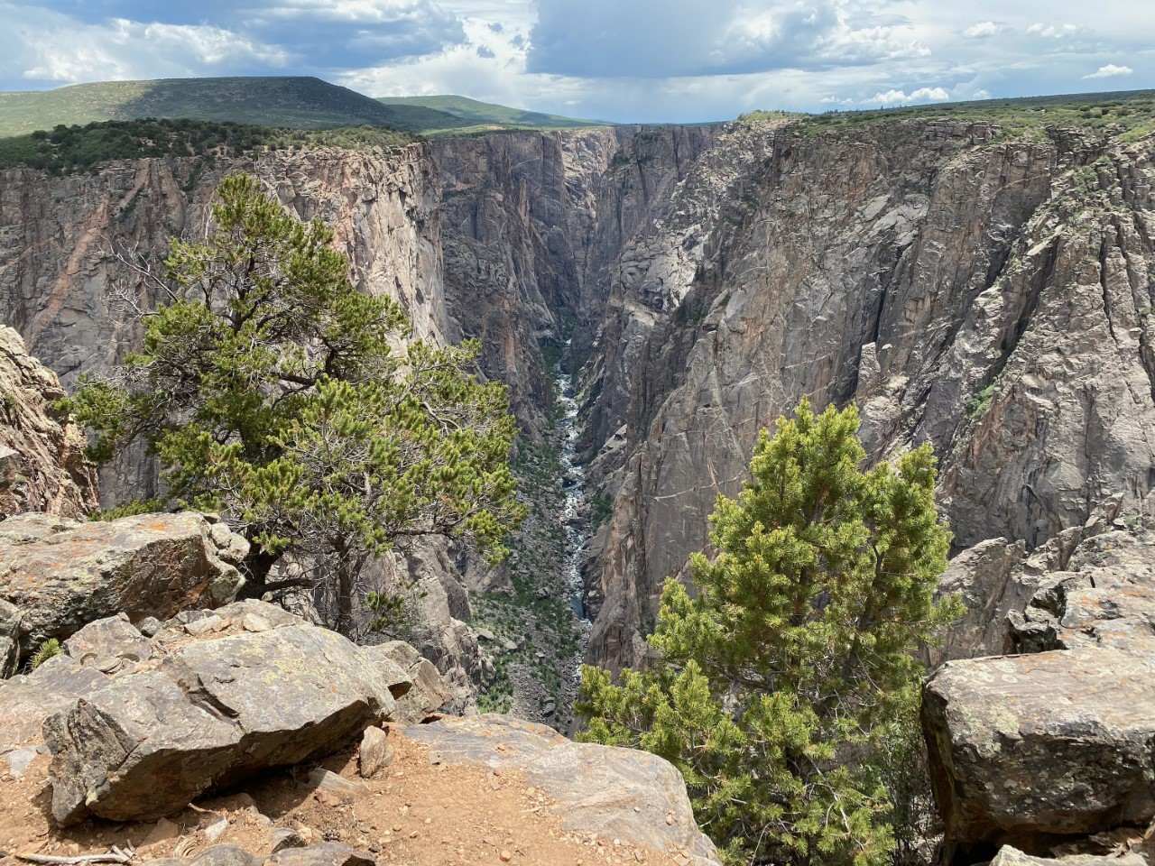 Canyon with rocky cliffs, greenery, and a river below under a partly cloudy sky.