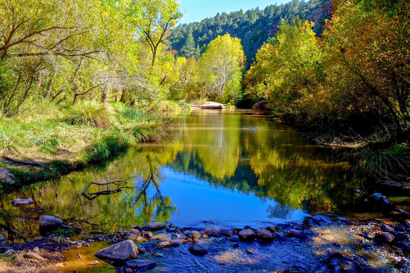 Tranquil river reflecting vibrant autumn trees and blue sky.