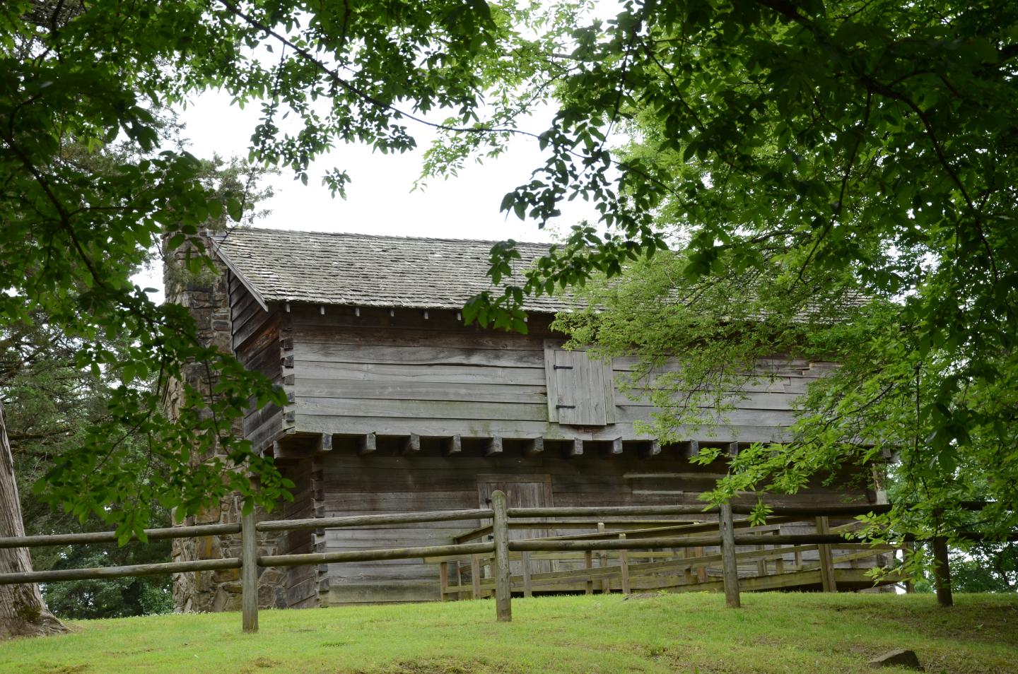 Historic wooden cabin surrounded by trees and a wooden fence.