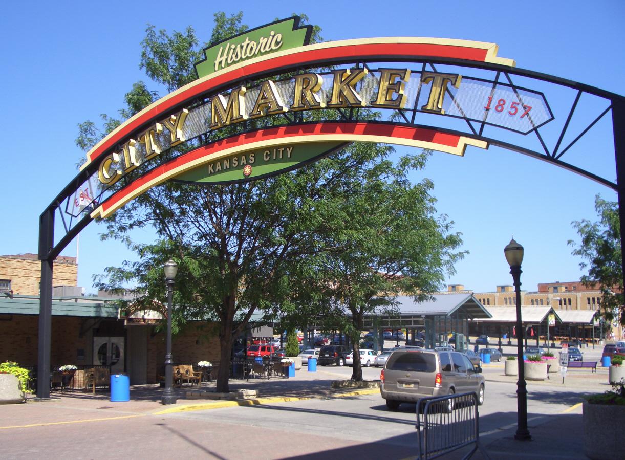 City Market entrance with archway, tree, and parked cars under a blue sky.