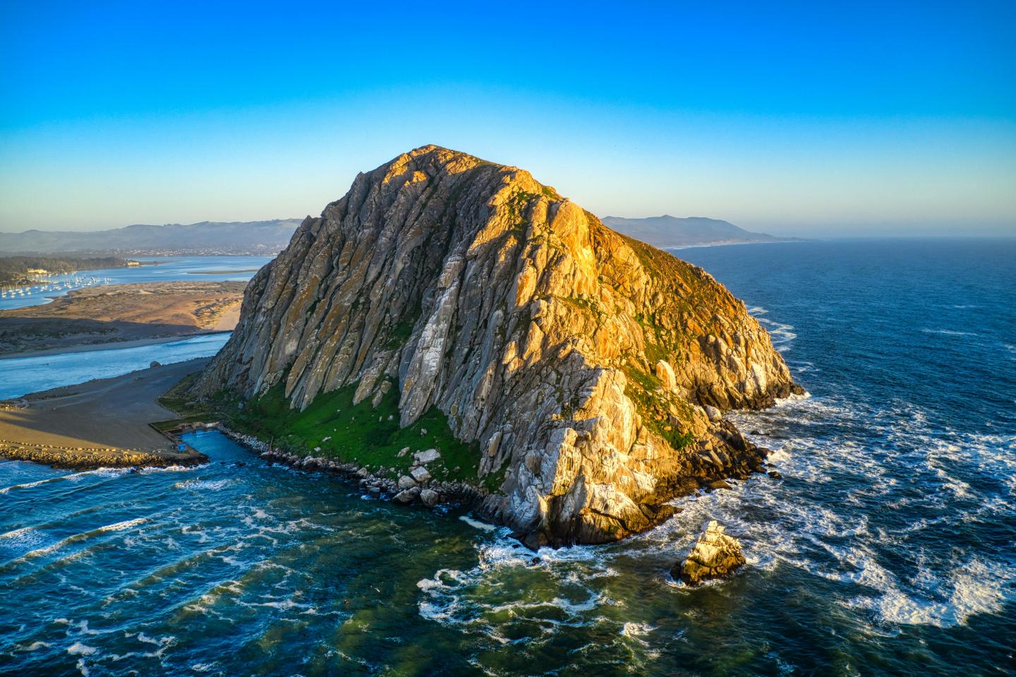 Rocky island in a blue ocean under clear sky at sunset.
