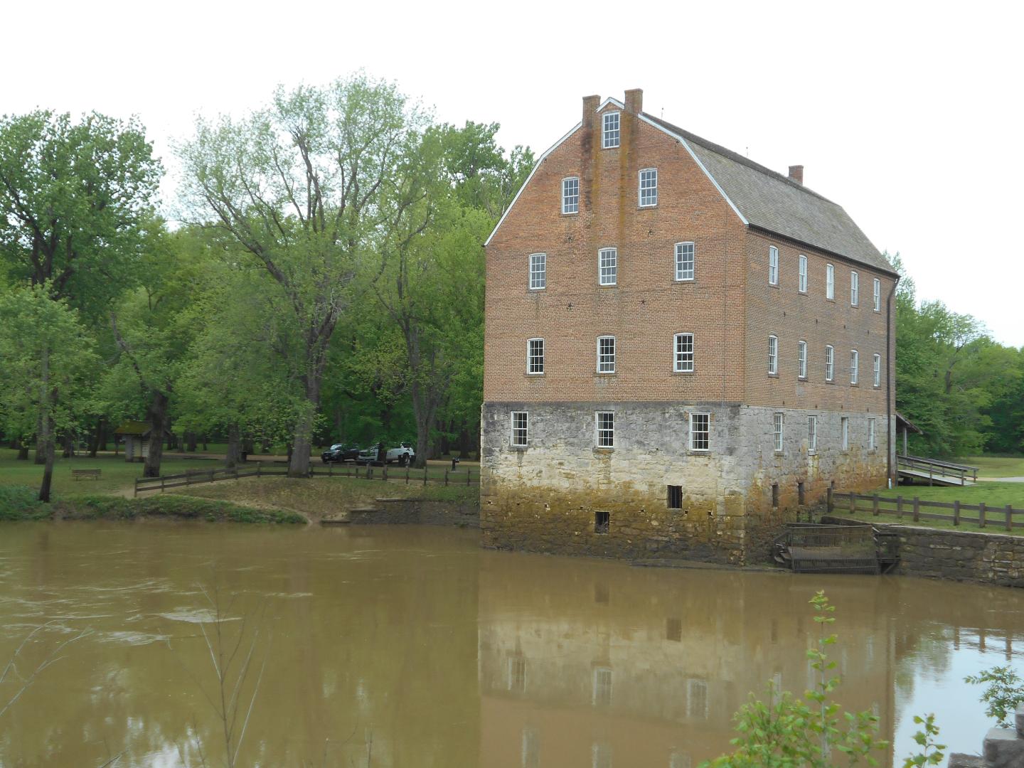 Historic brick mill by a river with trees in the background.