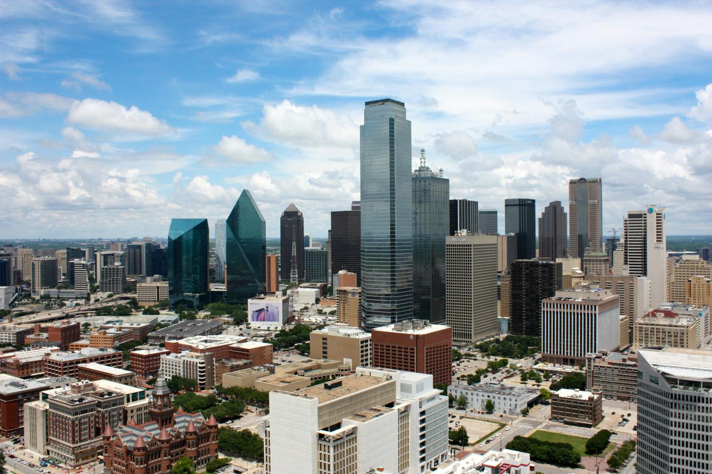 Dallas city skyline with tall skyscrapers under a blue sky with clouds.