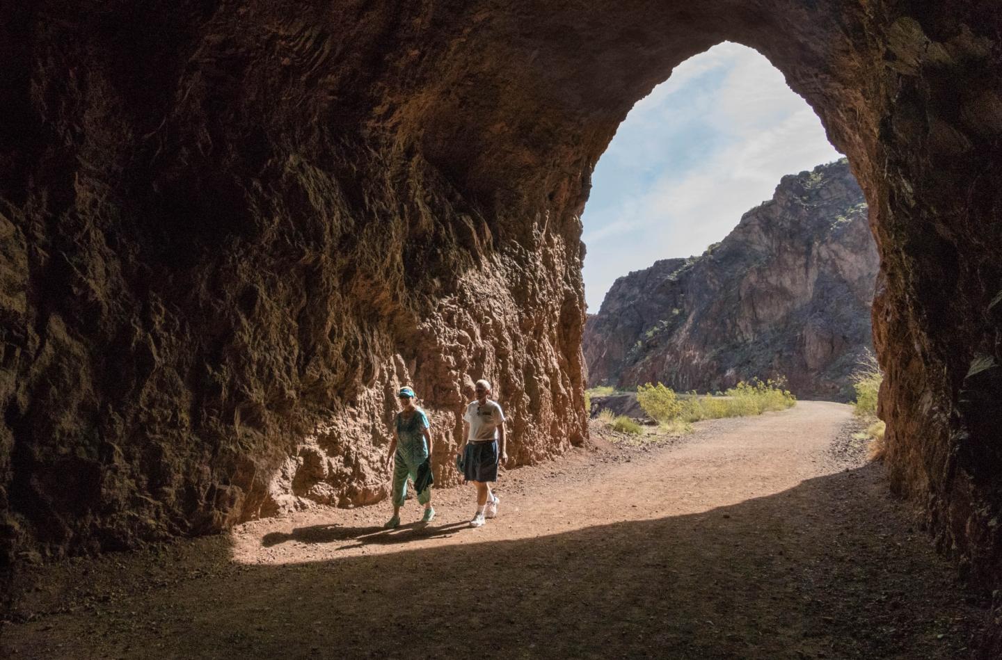 Two people inside a rocky cave, viewing the sunny landscape outside.