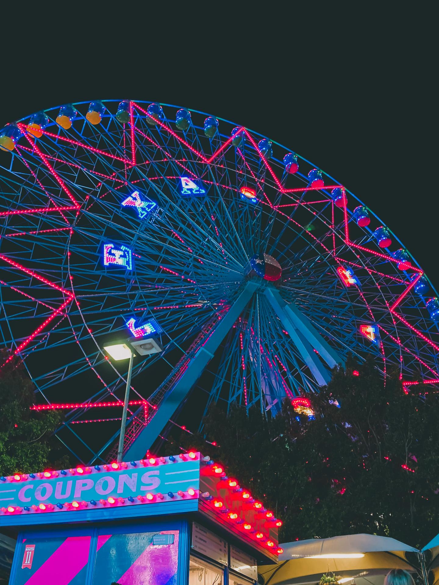 Ferris wheel lit with red and blue lights at night, with coupon booth below.